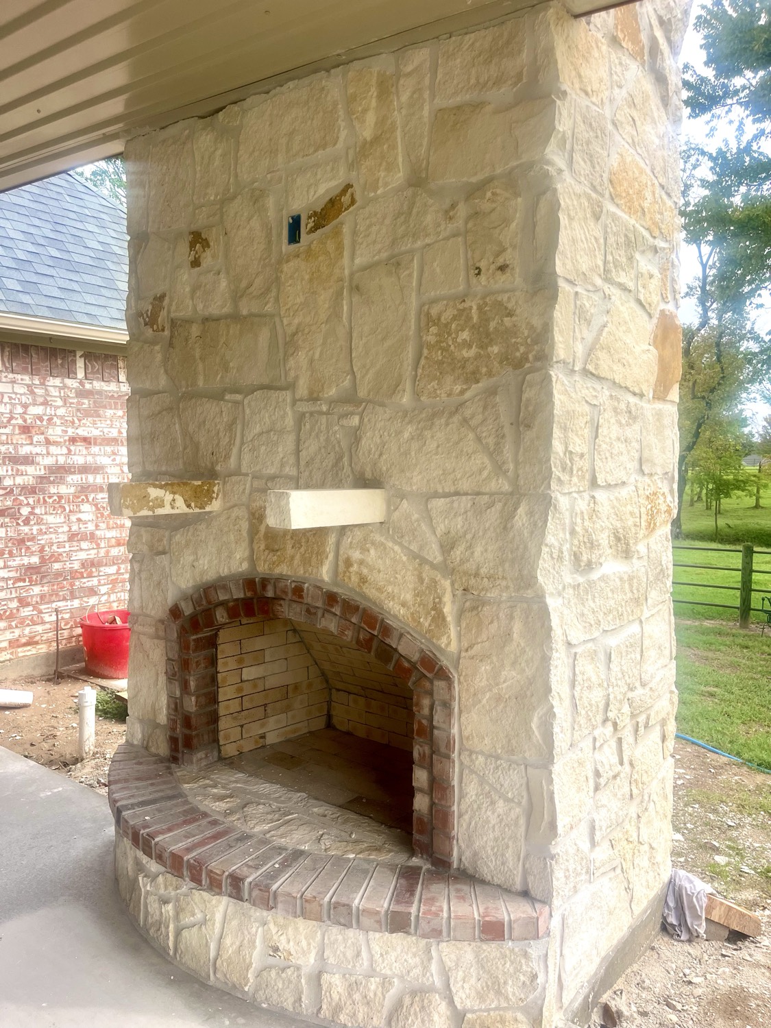 Outdoor stone fireplace with a brick-lined firebox on a covered patio